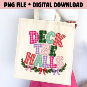 Op de afbeelding: Een crèmekleurige canvas tas met de tekst "DECK THE HALLS" in kleurrijke, gedessineerde letters in stofstijl. Het ontwerp bevat rode, groene, roze en paarse ruitjes, vichy-patronen en sneeuwvlokprints, geaccentueerd door een groene dennenkrans.