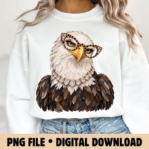 May include: A white crewneck sweatshirt featuring a graphic of a bald eagle wearing leopard print glasses and a sparkling rhinestone necklace. The eagle has detailed brown and white feathers, a yellow beak, and piercing eyes, centred on the chest.