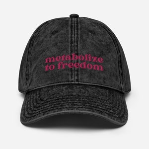 May include: A black vintage washed cotton baseball cap with the text "metabolize to freedom" embroidered in pink.