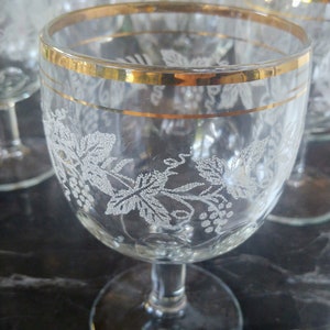 May include: Set of six clear glass wine glasses with a gold rim and etched grapevine design.