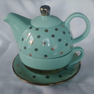 May include: A teal blue teapot and teacup set with gold polka dots. The teapot has a lid and a handle. The teacup has a handle and sits on a matching saucer.