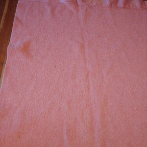 Op de afbeelding: Een roze wollen deken met een satijnen rand. De deken is zacht en pluche, en perfect om warm te blijven op een koude avond.