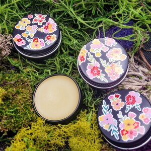 May include: Three small round tins with floral designs. The tins are filled with a pale yellow balm.
