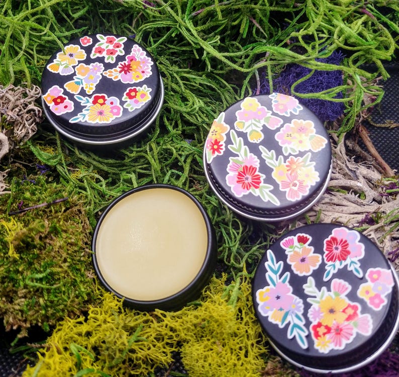 May include: Three small round tins with floral designs. The tins are filled with a pale yellow balm.