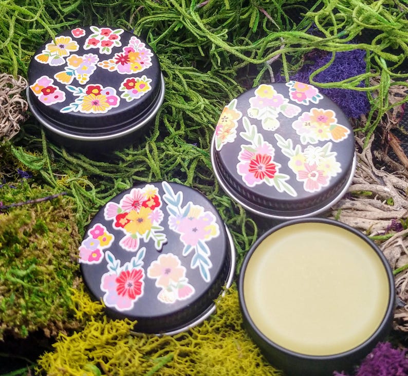 May include: Three small black tins with floral designs on the lids. One tin is open and contains a yellow balm.