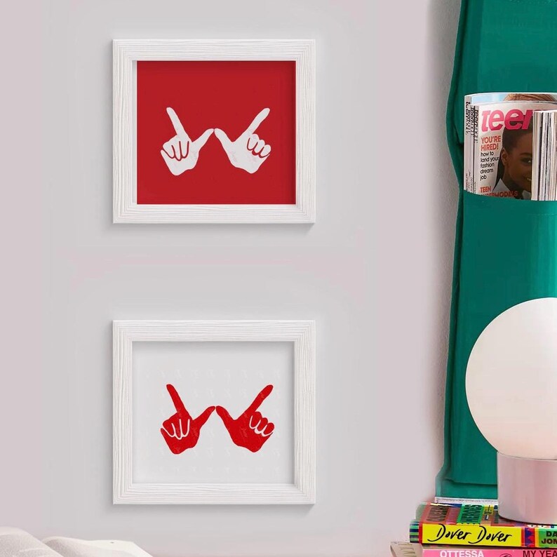 May include: Two white framed pictures with red and white backgrounds. The pictures feature a white hand gesture on a red background and a red hand gesture on a white background. The hand gesture is a peace sign with the index and pinky fingers extended.