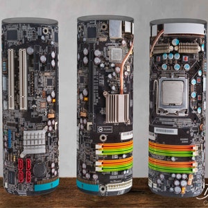 Puede incluir: Tres contenedores cilíndricos con un diseño impreso de una placa base de computadora. Los contenedores son negros con una variedad de componentes de colores, incluidos rojo, verde, azul y naranja.