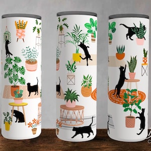 May include: Three white tumblers with black cats and green plants on a white background. The tumblers are on a wooden surface. Dover Creative Shop is printed on the bottom right tumbler.