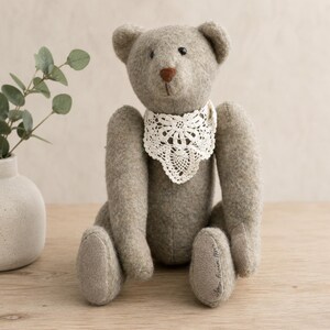 May include: A gray teddy bear with a white lace collar. The bear has a brown nose and black eyes. The bear is sitting on a wooden surface.