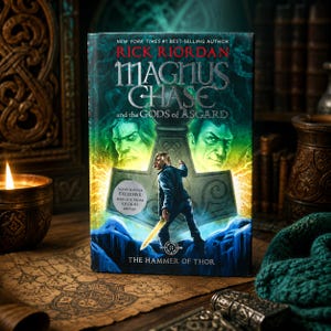 May include: A hardcover book titled "Magnus Chase and the Gods of Asgard: The Hammer of Thor" by Rick Riordan. The cover features a male figure with a sword, two green-faced figures, and the book's title. The book is on a map with a lit candle and a green scarf.