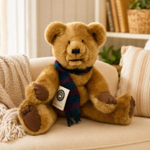May include: A plush brown teddy bear with a blue, green, and purple scarf. The bear has dark brown paws and a tag with a paw print logo. The bear is sitting on a beige couch.