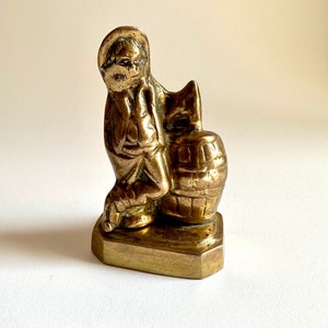 Peut inclure: Une figurine en laiton d'une personne tenant un tonneau. La figurine est debout sur une base carrée.