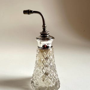 Puede incluir: Una botella de vidrio transparente con una tapa plateada y un largo pico curvo. La botella tiene un patrón de diamante en el vidrio. La botella está etiquetada como "Westminster Hall".
