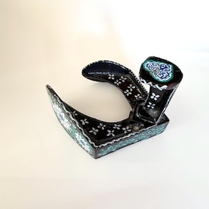 May include: A black, decorative object with a curved handle and a rectangular base. The object is adorned with white floral patterns and teal accents. The top features a teal and white heart-shaped design.