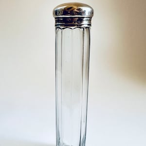 May include: A clear glass jar with a silver lid. The jar has vertical ridges and a rounded bottom. The lid has a smooth, shiny surface.