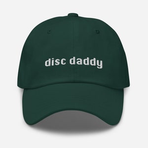 May include: A dark green baseball cap with the text "disc daddy" embroidered in white on the front.