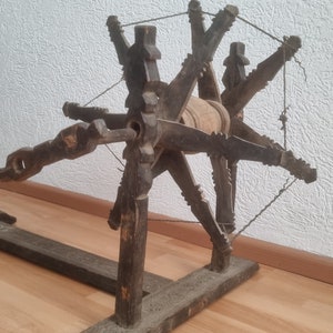 Puede incluir: Una rueca de madera con un acabado marrón oscuro y un huso de metal. La rueda tiene ocho radios y está montada sobre una base de madera.