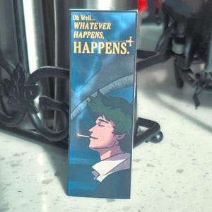 May include: A rectangular bookmark featuring an anime-style illustration of a person smoking a cigarette. The bookmark has the text "Oh Well... WHATEVER HAPPENS, HAPPENS." in gold lettering against a blue background.