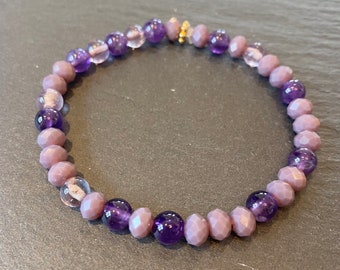 May include: A purple and gray beaded bracelet with a gold clasp. The bracelet is made with amethyst and faceted glass beads.