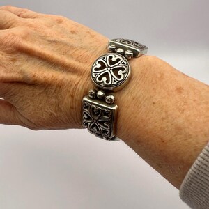 Puede incluir: Pulsera plateada con eslabones decorativos. La pulsera presenta eslabones cuadrados, redondos y rectangulares, cada uno adornado con patrones en forma de coraz&oacute;n. La pulsera est&aacute; dise&ntilde;ada para ser usada en la mu&ntilde;eca. El dise&ntilde;o es intrincado.