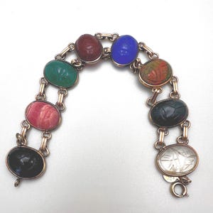 May include: A gold-toned bracelet featuring oval-shaped gemstones in various colors, including red, green, blue, and black. The gemstones are connected by gold links. The bracelet has a clasp closure.