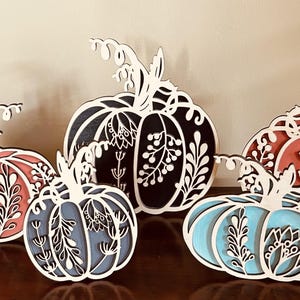May include: Four wooden pumpkins with intricate floral designs. The pumpkins are painted in shades of black, blue, pink, and red.