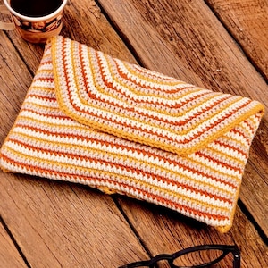 May include: A crocheted clutch bag with a striped pattern in orange, white, and beige. The bag is made with a textured stitch and has a flap closure.