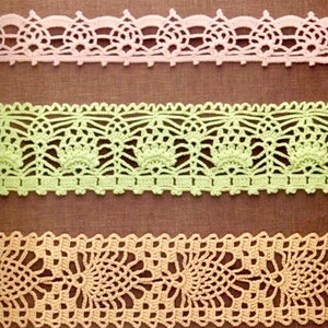 Puede incluir: Tres tipos diferentes de encaje de ganchillo en rosa, verde y beige. El encaje está dispuesto en una fila vertical sobre un fondo de tela marrón.