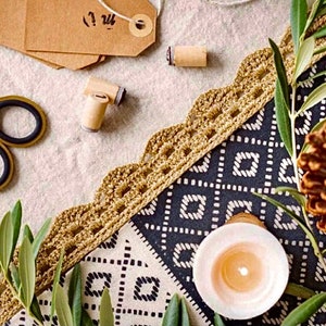 Puede incluir: Primer plano de una mesa puesta con un mantel estampado en blanco y negro, un ribete de encaje de ganchillo, una piña, una vela y follaje verde.