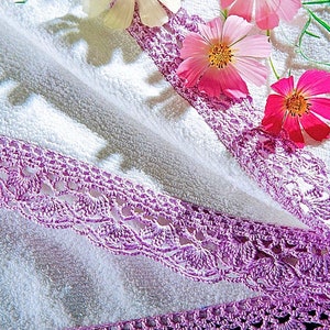 May include: A white towel with a purple crocheted lace border.  The towel is decorated with pink and white flowers.