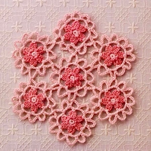 May include: A handmade, pink crocheted doily featuring a floral design. The doily is composed of six pink flowers with a darker pink center, connected by a delicate, openwork pattern. The overall design is symmetrical and intricate.