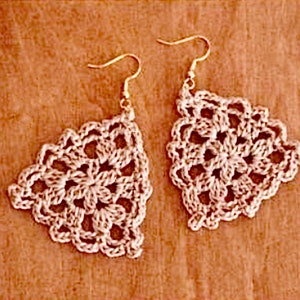 May include: A pair of crocheted earrings in a delicate, intricate pattern. The earrings are triangular in shape and feature a white color.