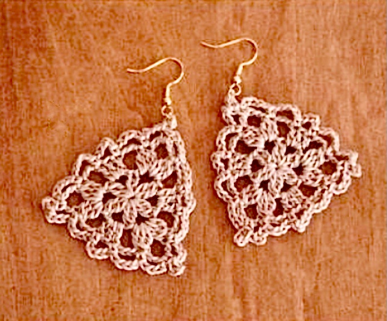 May include: A pair of crocheted earrings in a delicate, intricate pattern. The earrings are triangular in shape and feature a white color.