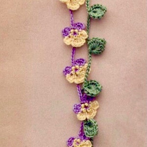 Könnte beinhalten: Ein gehäkeltes Armband mit einer Kette aus gelben und violetten Blumen und grünen Blättern.
