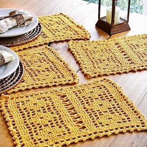 Puede incluir: Cuatro manteles individuales de crochet amarillos sobre una mesa de madera. Los manteles individuales tienen un diseño delicado y calado.