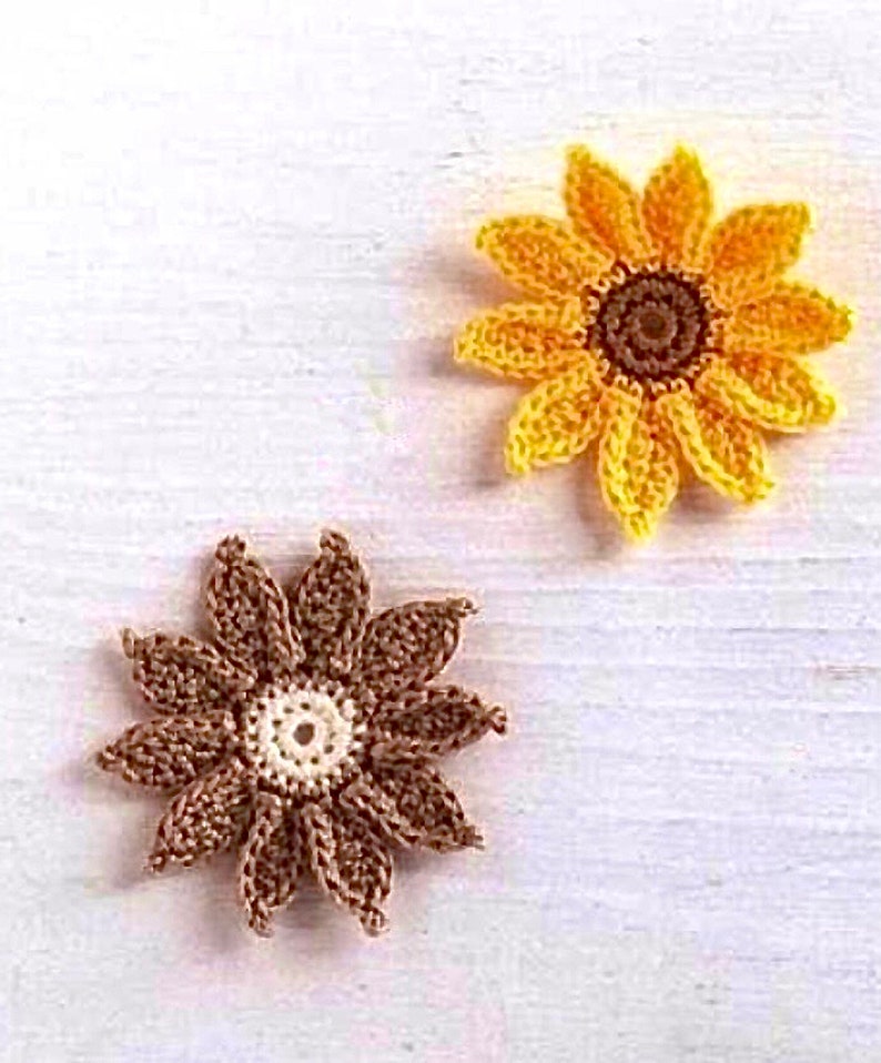 Puede incluir: Dos flores de ganchillo en forma de girasol. Una flor es marr&oacute;n con un centro blanco, y la otra es amarilla con un centro marr&oacute;n.