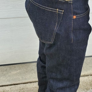 May include: Dark blue denim jeans with yellow stitching and a leather patch that reads "Copper Overalls Riveted For Ever." The jeans have a W29 size label and orange rivets.