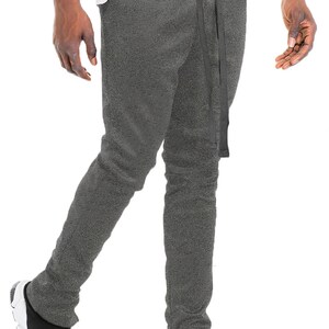 May include: Gray sweatpants with a drawstring and side slits. The pants are paired with black and white sneakers. The model is wearing a white t-shirt.