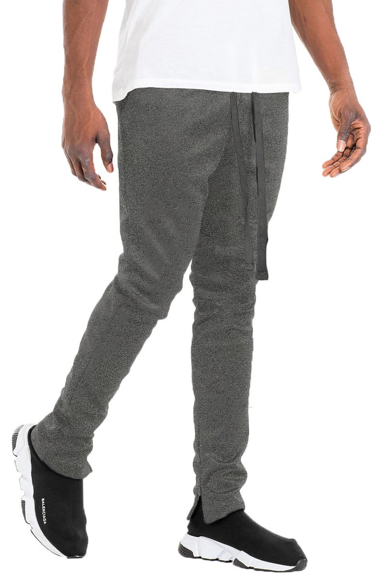 May include: Gray sweatpants with a drawstring and side slits. The pants are paired with black and white sneakers. The model is wearing a white t-shirt.