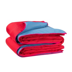 May include: A folded red and blue blanket with pink trim. The blanket is folded in thirds, with the blue side facing up.