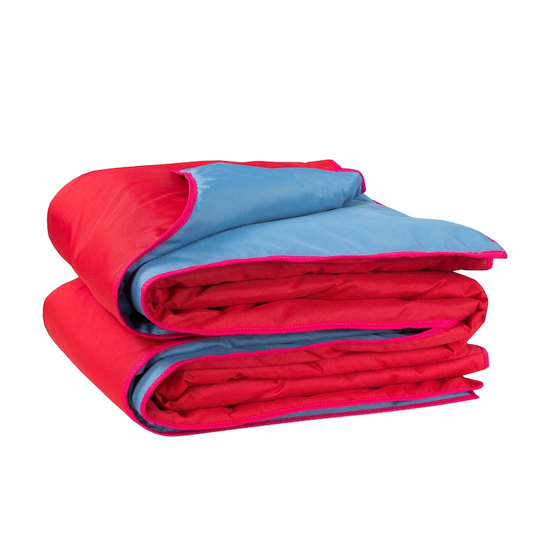 May include: A folded red and blue blanket with pink trim. The blanket is folded in thirds, with the blue side facing up.