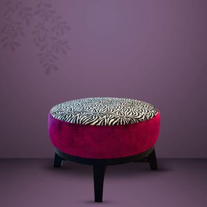 Op de afbeelding: Een ronde poef met een zwart-witte zebraprint op de bovenzijde. De zijkanten van de poef zijn bekleed met een effen, diep magenta fluwelen stof. Het meubelstuk rust op vier korte, stevige zwarte houten poten.
