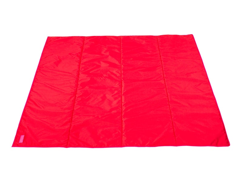 May include: A bright red quilted picnic blanket. The blanket is folded in half and has a pink label on the bottom left corner.