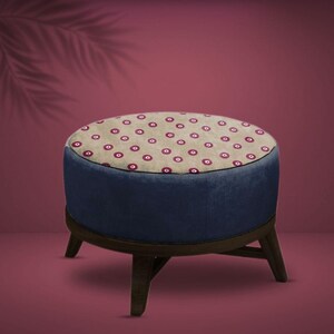Può includere: Un pouf rotondo, blu e beige con un motivo a pois rossi sulla parte superiore. Il pouf ha quattro gambe in legno.
