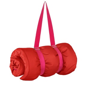 May include: A red sleeping bag rolled up with pink straps and buckles. The straps are attached to the bag and can be used to carry it.