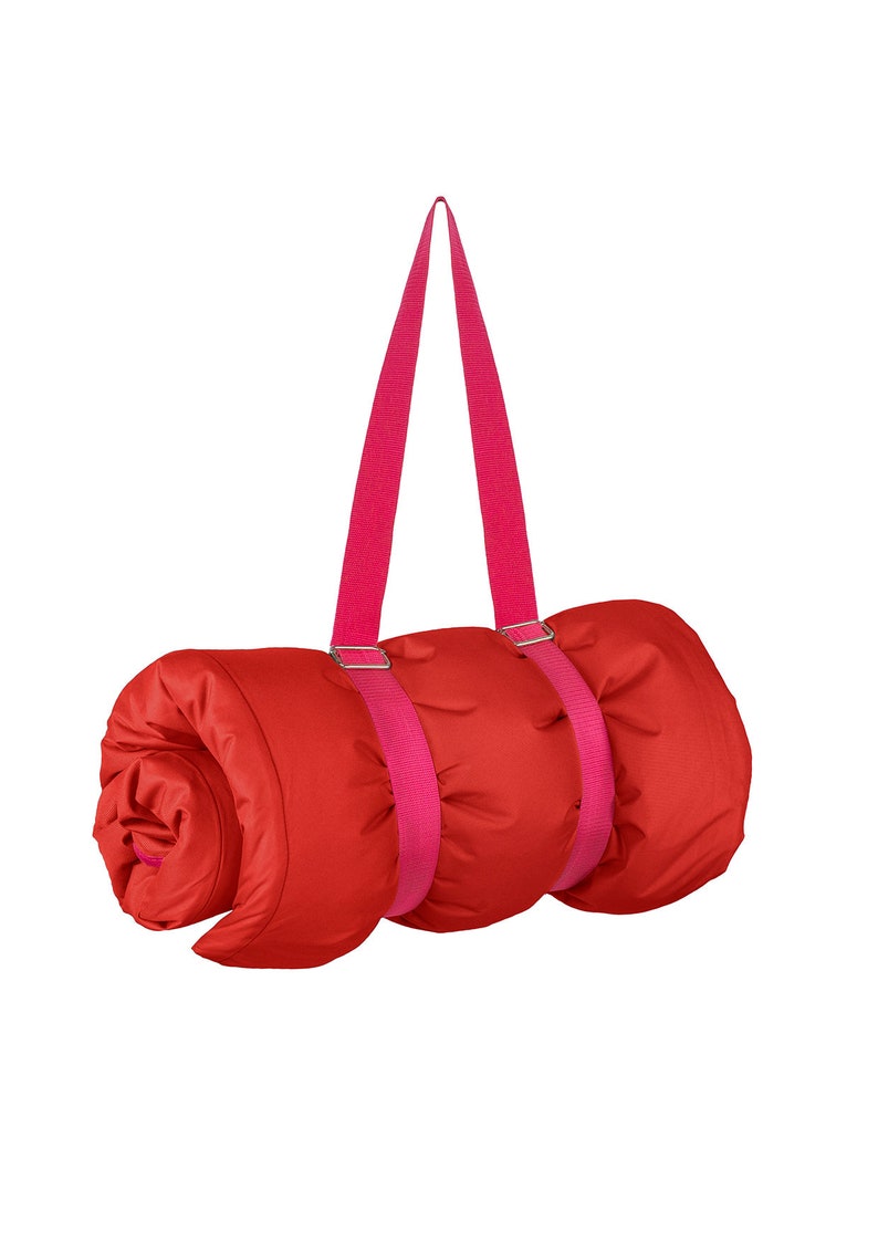 May include: A red sleeping bag rolled up with pink straps and buckles. The straps are attached to the bag and can be used to carry it.