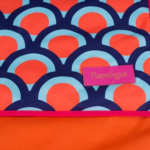 Puede incluir: Una tela con estampado azul y naranja con una etiqueta rosa que dice "Flamingos".