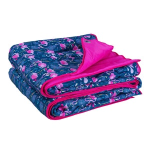 Puede incluir: Una manta azul y rosa con estampado doblada con un lado inferior rosa. La manta presenta un diseño de flamencos.