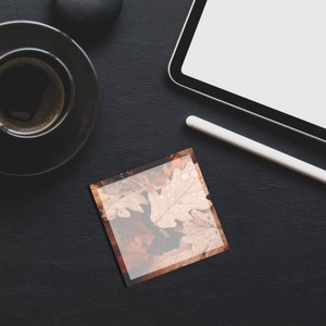 May include: A flat lay of a black leather desk with a cup of coffee, a tablet, a stylus, and a square card with a photo of autumn leaves.