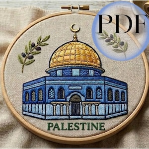 Puede incluir: Arte bordado en bastidor que representa la Cúpula de la Roca en Jerusalén. El edificio es azul y dorado, con una luna creciente en la parte superior. La palabra "PALESTINE" está bordada en la parte inferior, y ramas de olivo a la izquierda.